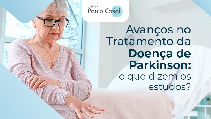 
Mulher idosa com as mãos trêmulas observando seus braços, com texto sobre avanços no tratamento da Doença de Parkinson, exibido pela Clínica Paulo Casali.