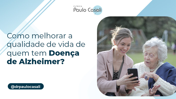 Como melhorar a qualidade de vida de quem tem Doença de Alzheimer? 1 Mulher jovem e idosa sentadas em um banco ao ar livre, sorrindo enquanto olham para um celular, simbolizando conexão e aprendizado intergeracional.