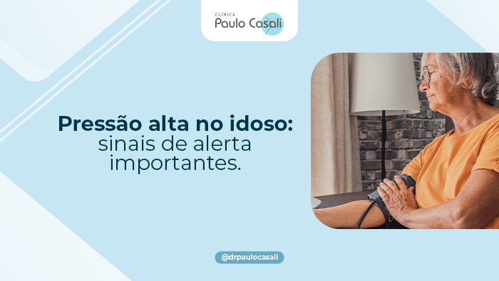 Idosa mede a pressão arterial em casa com aparelho no braço, sentada ao lado de uma luminária.