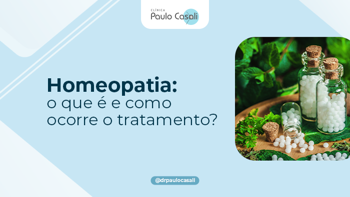 Frascos de vidro contendo pequenos glóbulos brancos sobre bandeja de madeira, cercados por folhas verdes, ervas e plantas.